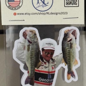 May include: Sticker featuring a man holding two large fish. The man is wearing a racing uniform and a hat. The sticker has the text "STICKERS by RL Designs" and "Made in USA".
