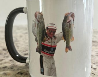 Può includere: Una tazza in ceramica bianca con un manico nero e un'immagine stampata di un uomo che tiene due grossi pesci. L'uomo indossa una tuta da corsa rosso, bianco e blu con le parole "Goodwrench" stampate.