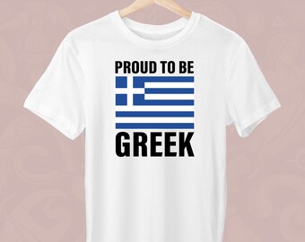 Peut inclure: T-shirt blanc avec l'inscription "PROUD TO BE GREEK" en noir, surmontant un drapeau grec bleu et blanc. Le t-shirt est suspendu à un cintre en bois. Le fond est rose clair. Vêtement décontracté et patriotique.