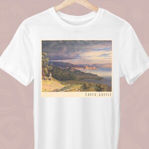 May include: A white t-shirt featuring a vintage postcard print of a scenic landscape. The postcard depicts a view of a body of water with a mountainous coastline in the distance. The text on the postcard reads "Corfu, Greece".
