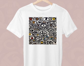Peut inclure: T-shirt blanc avec un motif carré d'yeux stylisés de différentes couleurs, dont le rouge, le jaune et le bleu. Les yeux sont placés sur un fond blanc, créant un motif saisissant. Le t-shirt est suspendu à un cintre en bois.