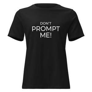 May include: Black t-shirt with the white text "DON'T PROMPT ME!". The short-sleeved shirt is made of a soft material and has a crew neck. The text is centered on the front of the shirt.