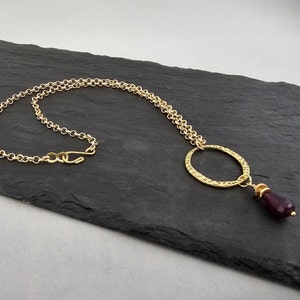 May include: A gold chain necklace with a hammered gold circle pendant and a dangling purple gemstone.