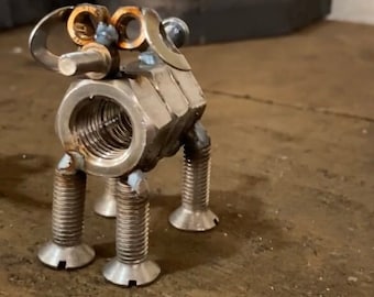 May include: A small, silver metal sculpture of a dog made from nuts, bolts, and screws. The dog is standing on four legs and has a long tail.