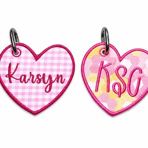 May include: Two heart-shaped keychains. One features a pink and white gingham pattern with the name "Karsyn" in cursive. The other has a pink and yellow honeycomb pattern with the initials "KSG". Both have a pink border and a silver metal ring.