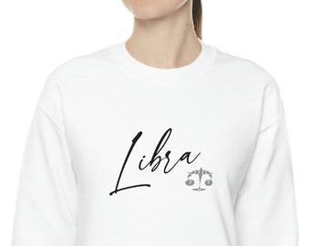 Op de afbeelding: Witte trui met zwarte tekst "Libra" en een grijs Libra sterrenbeeld symbool.