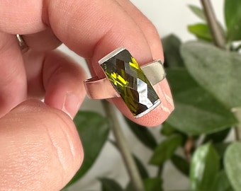 May include: A silver ring featuring a large, rectangular, faceted green gemstone.
