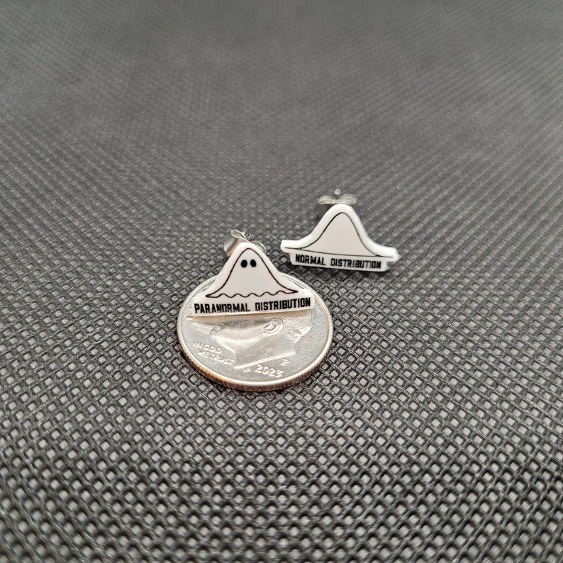 May include: A pair of silver stud earrings with a ghost-shaped design. One earring says "Paranormal Distribution" and the other says "Normal Distribution".
