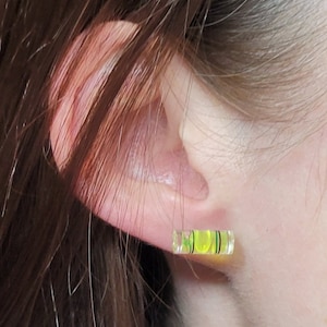 May include: A pair of yellow and green level earrings. The earrings are shaped like a small level and have a black line in the middle.