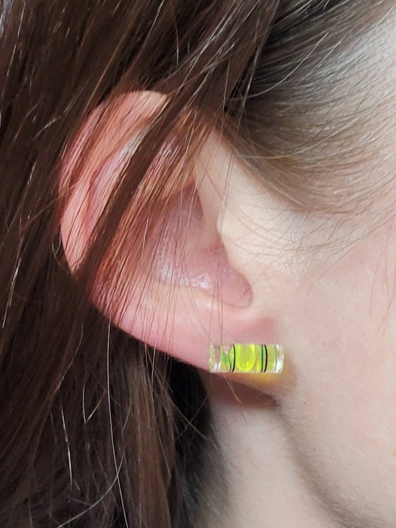 May include: A pair of yellow and green level earrings. The earrings are shaped like a small level and have a black line in the middle.