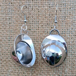 May include: A pair of silver earrings shaped like hard hats. The earrings are hanging from a brown burlap background.
