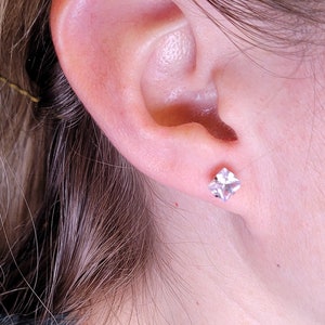 Op de afbeelding: Een close-up van iemands oor met een kleine, vierkante, doorzichtige oorbel.