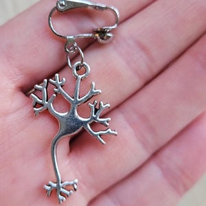 Op de afbeelding: Zilveren clip-on oorbel met een gedetailleerd anatomisch ontwerp van een neuron, een zenuwcel.