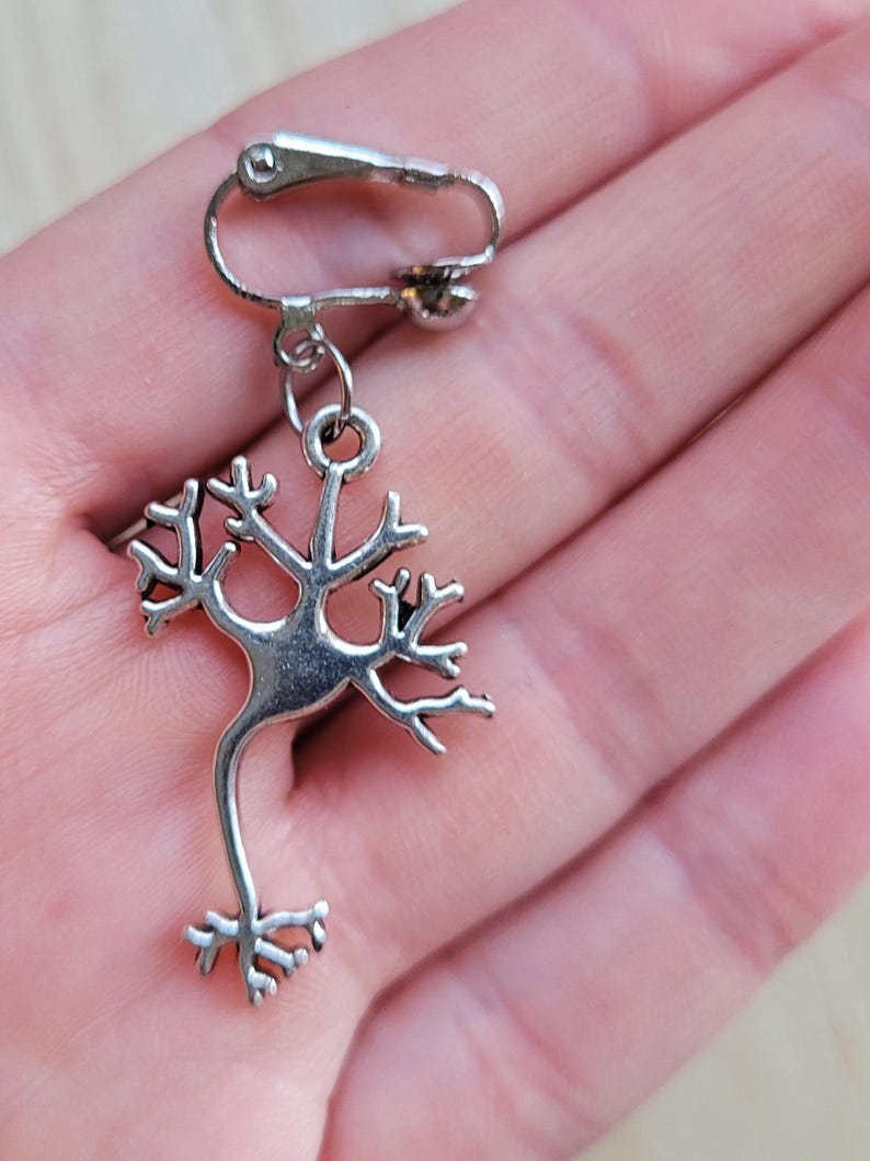 Op de afbeelding: Zilveren clip-on oorbel met een gedetailleerd anatomisch ontwerp van een neuron, een zenuwcel.