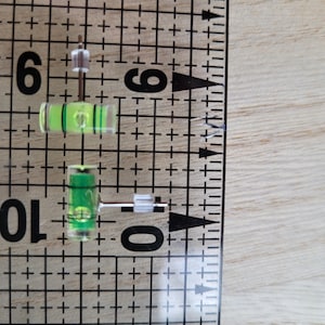 May include: Two small green and clear levelers with a white plastic base. The levelers are about 1 inch long and are sitting on a white grid.