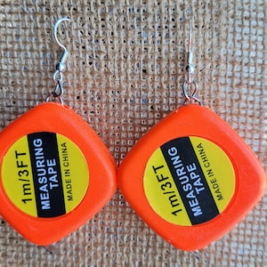May include: A pair of orange measuring tape earrings with silver hooks. The tape measures 1 meter or 3 feet and is labeled "Made in China".