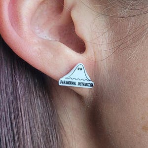 May include: White ghost-shaped earring with the text "Paranormal Distribution" in black lettering.