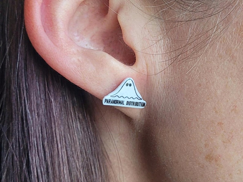 May include: White ghost-shaped earring with the text "Paranormal Distribution" in black lettering.