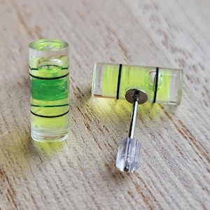 May include: A pair of clear glass level earrings with a green liquid inside. The earrings are attached to silver posts with clear plastic stoppers.