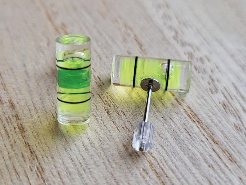 May include: A pair of clear glass level earrings with a green liquid inside. The earrings are attached to silver posts with clear plastic stoppers.
