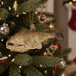Puede incluir: Un &aacute;rbol de Navidad decorado con adornos tem&aacute;ticos de pesca, incluyendo un pez, se&ntilde;uelos, un peque&ntilde;o barco y bolas brillantes. El &aacute;rbol est&aacute; iluminado con peque&ntilde;as luces blancas, creando una escena festiva navide&ntilde;a.