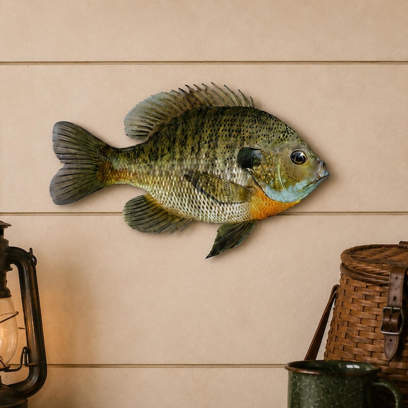 K&ouml;nnte beinhalten: Eine dekorative Fischfigur zur Wandmontage mit einem gesprenkelten olivgr&uuml;nen und braunen K&ouml;rper, einem markanten dunklen Fleck am Kiemendeckel, einem hellblau get&ouml;nten Wangenbereich und einem leuchtend orange-gelben Fleck am unteren Bauch.