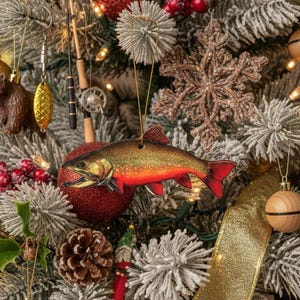Könnte beinhalten: Ein Weihnachtsbaum, der mit Angel-Themen-Ornamenten geschmückt ist. Ein Holzfisch-Ornament mit roten und goldenen Farben hängt in der Nähe einer roten Glitzerkugel. Weitere Ornamente sind Angelruten, Köder und ein Holzbär.