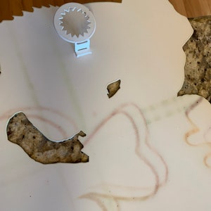 May include: A white, cut-out decorative wall hanging with a floral design. The piece has a white plastic sawtooth hanger attached to the back. Faint, colourful lines outline the floral shapes.