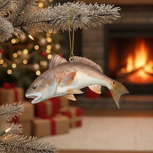 May include: A detailed Christmas tree ornament shaped like a redfish. The ornament is a realistic depiction of the fish, with a light brown body, white belly, and orange fins. It hangs from a gold string, perfect for a fishing enthusiast's holiday decor.