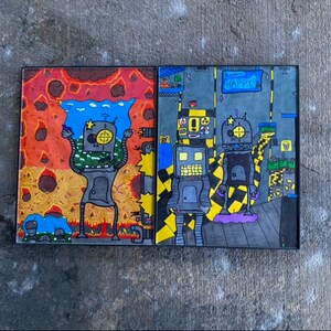 Può includere: Due dipinti incorniciati di robot in ambientazioni diverse. Il dipinto a sinistra mostra un robot in un paesaggio infuocato con la parola "Happy!" su uno striscione blu. Il dipinto a destra mostra un robot in un ambiente industriale con un pavimento a scacchi giallo e nero.