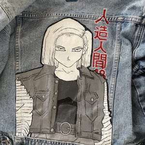 May include: Light blue denim jacket featuring a hand-painted illustration of an anime character. The artwork depicts a woman with short blonde hair and a black and gray outfit. Japanese text is visible on the upper right side of the jacket.