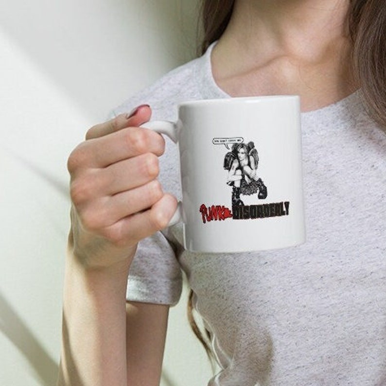 May include: White ceramic mug featuring a black and white illustration of a figure with the text "YOU WON'T CATCH ME" in a speech bubble. Below the illustration is the text "PUNK DISORDERLY" in red and black.