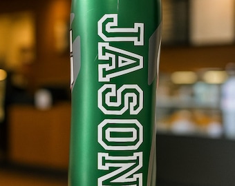 May include: A green water bottle with an orange lid. The word "JASON" is printed vertically in white, bold letters on the front of the bottle. The bottle is cylindrical and appears to be made of metal.