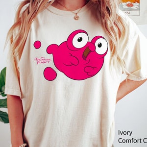 May include: A white t-shirt featuring a pink cartoon character from Disney's Treasure Planet. The character is a pink blob with a mouth and eyes. The text "Disney Treasure Planet" is printed on the shirt.