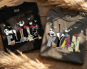 May include: Two crewneck t-shirts, one black and one dark grey, featuring custom graphic designs. The black shirt displays the name ELLIE and the grey shirt displays the name RYAN, both decorated with characters, pumpkins, and bats.