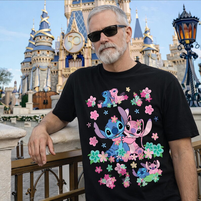 May include: Black t-shirt featuring a colorful graphic of Stitch and Angel surrounded by pink, blue, and green flowers. The design includes multiple images of the characters. The background shows a castle.