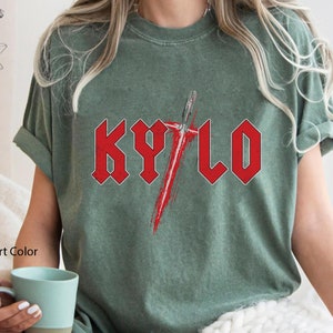May include: A moss green t-shirt featuring a red graphic of the word "KYLO" in a heavy metal font with a red lightsaber behind it.
