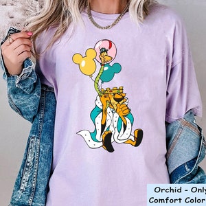 May include: A purple t-shirt with a cartoon image of a king holding balloons. The balloons are yellow, blue, and pink. The text "Orchid - Only For Comfort Color Shirt" is at the bottom of the image.