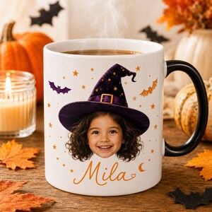 May include: A white ceramic mug with a black handle featuring a printed graphic of a child wearing a purple witch hat with gold stars. The design includes orange stars, bats, and the name Mila in orange script text below the child's portrait.