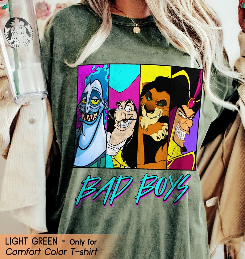 May include: Light green Comfort Color T-shirt featuring a graphic of four cartoon villains in colorful panels. The words "BAD BOYS" are printed in turquoise with a purple outline. The shirt is a relaxed fit.