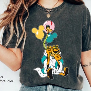 May include: A black t-shirt with a cartoon lion wearing a crown and holding balloons. The balloons are yellow, blue, and pink. The lion is wearing a blue and white robe. The text "More Ocean" is written on the right sleeve of the shirt.