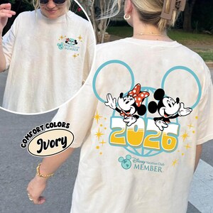 May include: Ivory t-shirt featuring Mickey and Minnie Mouse graphic, the number "2025", and the text "Disney Vacation Club Member". The shirt has a crew neck and short sleeves. The front of the shirt has a smaller graphic.