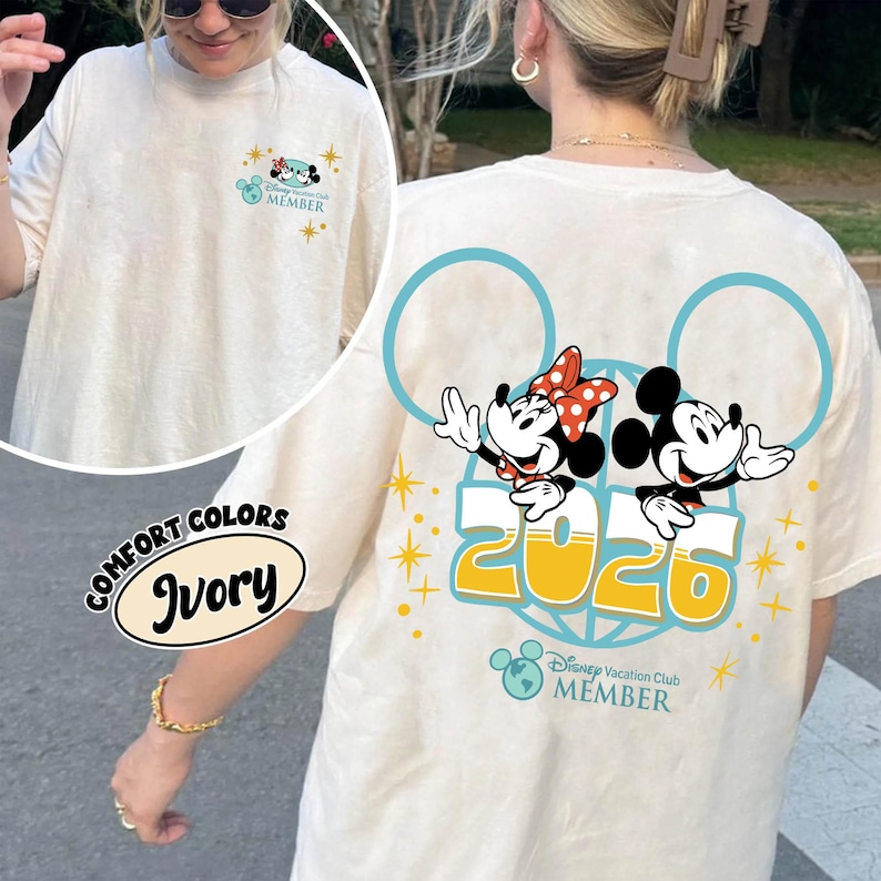 May include: Ivory t-shirt featuring Mickey and Minnie Mouse graphic, the number "2025", and the text "Disney Vacation Club Member". The shirt has a crew neck and short sleeves. The front of the shirt has a smaller graphic.