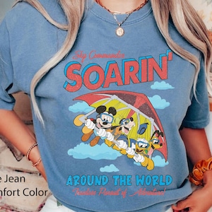 Puede incluir: Una camiseta azul vaquero con un gr&aacute;fico de Mickey Mouse y sus amigos volando en un ala delta. El texto "Soarin' Around the World" est&aacute; impreso en la camiseta.