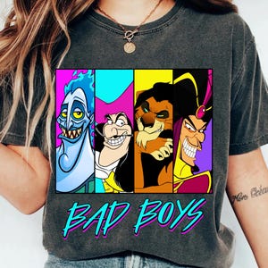 May include: Dark gray t-shirt featuring a graphic of four cartoon villains: Hades, Captain Hook, Scar, and Jafar. The text "BAD BOYS" is printed in turquoise and pink below the graphic. The shirt is a casual style.