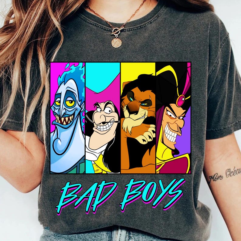 May include: Dark gray t-shirt featuring a graphic of four cartoon villains: Hades, Captain Hook, Scar, and Jafar. The text "BAD BOYS" is printed in turquoise and pink below the graphic. The shirt is a casual style.