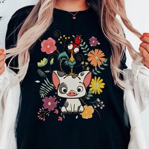 Pu&ograve; includere: Maglietta nera con un'immagine di un maiale e un gallo in stile cartone animato circondati da fiori colorati.