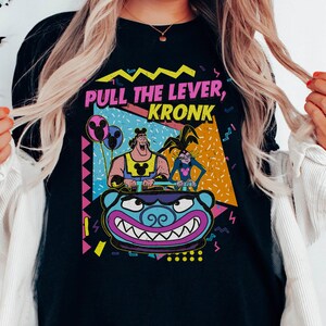 Puede incluir: Camiseta negra con un dise&ntilde;o retro de los 90 con los personajes Kronk e Yzma de la pel&iacute;cula de Disney El Emperador y sus locuras. El texto de la camiseta dice "Pull the Lever, Kronk".