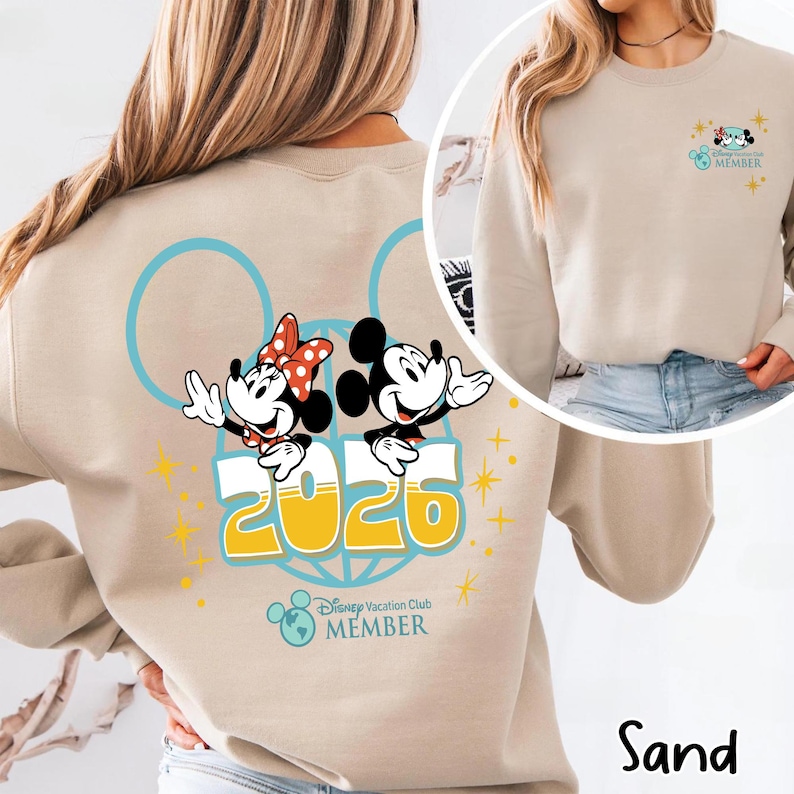 May include: Sand-coloured sweatshirt with Mickey and Minnie Mouse, the year "2026", and "Disney Vacation Club MEMBER". The design includes blue circles and yellow starbursts. A smaller version of the design is on the upper right.