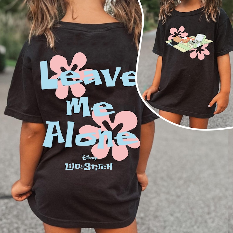 Puede incluir: Camiseta negra con la frase "Leave Me Alone" en texto azul claro, detalles de flores rosas y el logotipo de Disney Lilo & Stitch. Una imagen m&aacute;s peque&ntilde;a muestra un personaje de dibujos animados en la parte delantera.